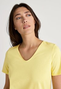 Gelbes kurzärmliges T-Shirt mit V-Ausschnitt, aus weichem Stoff gefertigt, mit glatter Textur und minimalistischer Gestaltung.