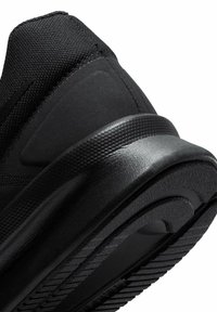 Gros plan de l'arrière et de la semelle d'une basket noire montrant un talon texturé et des détails de la semelle intermédiaire amortie.