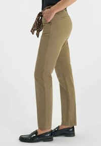 Pantalon kaki avec une taille ceinturée et un nœud en imprimé léopard, poches latérales, coupe fuselée et tissu lisse. Porté avec des mocassins noirs.