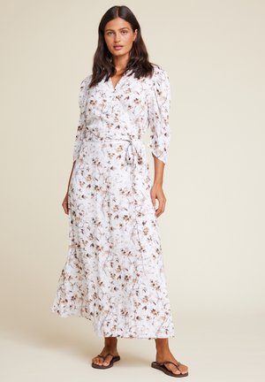 Maxi omslagskjole i hvit med blomstertrykk i brune nyanser. Har lange ermer, en knyting i midjen og en luftig silhuett.