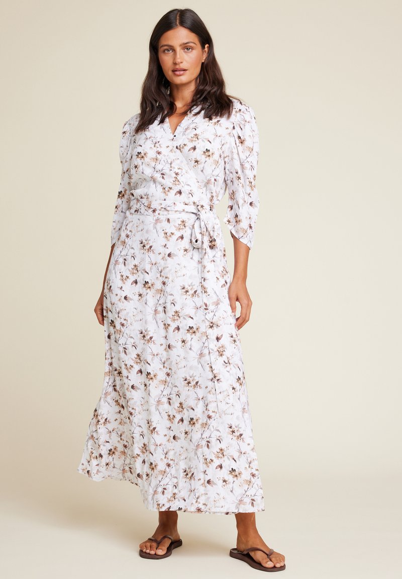 Maxi omslagskjole i hvit med blomstertrykk i brune nyanser. Har lange ermer, en knyting i midjen og en luftig silhuett.