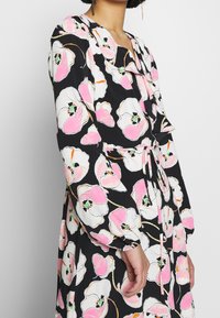 Svart blommig klänning med stora rosa blommor och gröna detaljer. Långa ärmar med elastiska manschetter och ett midjeband för justering.