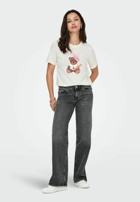 Hvid T-shirt med et tegneserie-bjørne grafik, grå brede bukser og hvide sneakers. T-shirten har lyserøde accenter og et legende design.