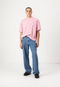 Pink short-sleeve textured t-shirt with pattern detailing, paired with light blue wide-leg cargo jeans and black sneakers.