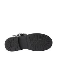 Suela de zapato negro con un patrón de relieve profundo, detalles de hebilla y texto "Hecho en España" en el centro inferior.