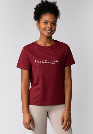 Burgunderfarbener Baumwoll-T-Shirt mit kurzen Ärmeln und weißem Text "Alle Jahre wieder..." auf der Vorderseite. Glatte Textur, klassischer Schnitt.