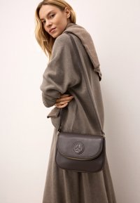 Borsa a tracolla in pelle marrone con chiusura a zip e logo impresso, dotata di una lunga tracolla regolabile e un design liscio e strutturato.