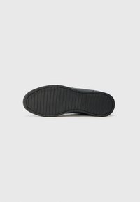 Schwarze Sneaker-Sohle aus strukturiertem Gummi mit horizontalen und vertikalen Rillen für besseren Halt. Glatte obere Kante und dezente Logo-Details.