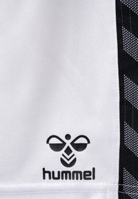 Hvidt stof med en tekstureret overflade, der har et sort Hummel-logo og et sort geometrisk mønster på højre side.