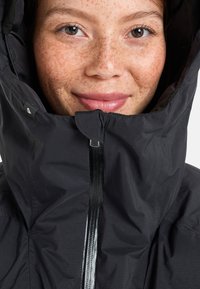Black waterproof jacket featuring a high collar and zip closure. The material has a slight sheen, with a gathered hood and smooth texture.