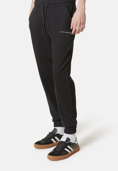 Pantaloni della tuta neri con design affusolato, dotati di vita elasticizzata e cordino. Accentuati dal logo "RICHMOND" in bianco. Abbinati a sneaker nere.
