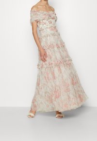 Off-shoulder blommig klänning i mjukt, lätt tyg med rosa och gröna mönster. Har volanglager och en svävande siluett.