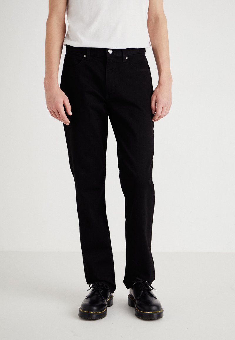 Black denim pants with a straight leg design, featuring front pockets and a button closure. Worn with a white t-shirt and black shoes.
