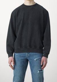 Tmavě šedá, nadměrně velká mikina s kulatým výstřihem a dlouhými rukávy. Měkká textura, žebrované manžety a lem. Kombinováno se světle modrými roztrhanými džíny.