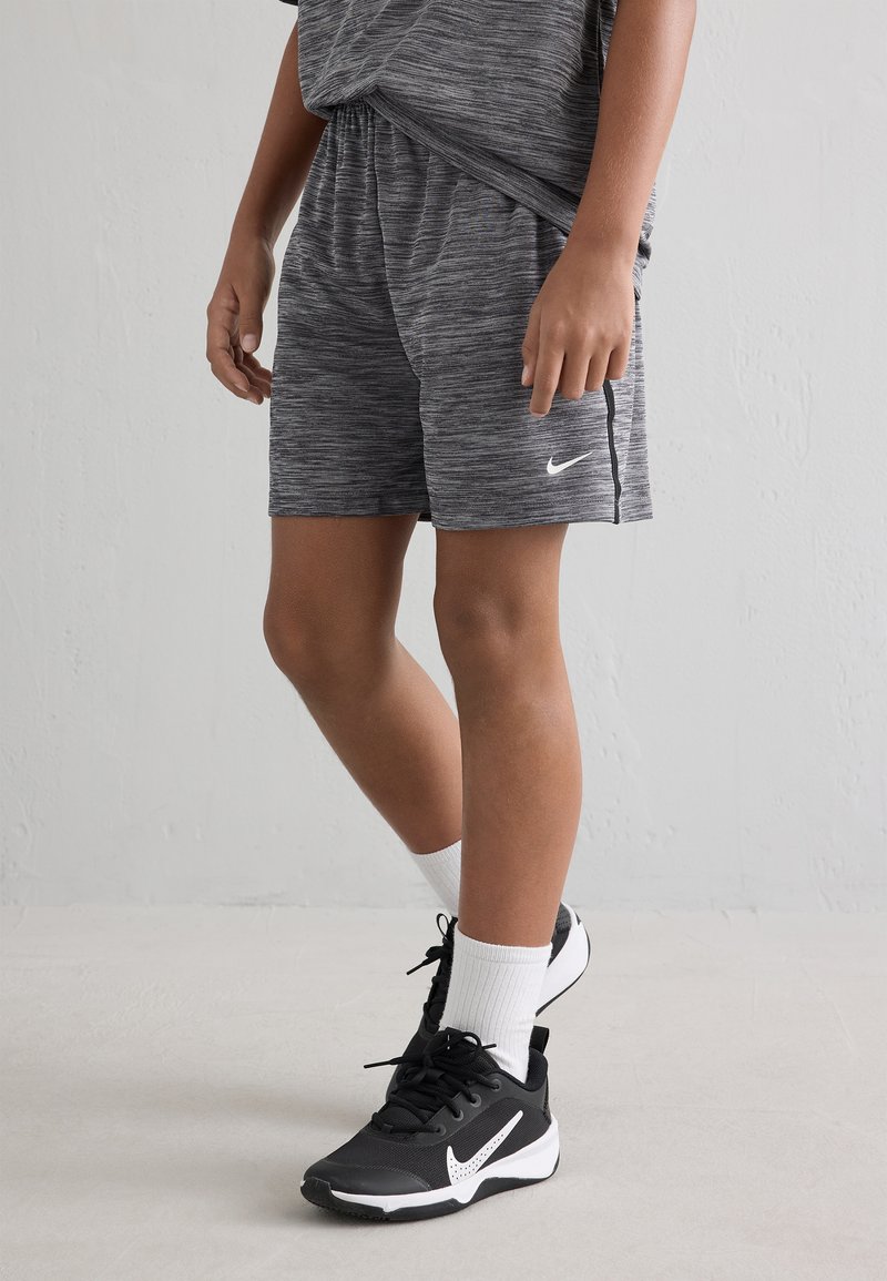 Pelēki sporta šorti ar teksturētu rakstu un elastīgu jostasvietu, apvienoti ar melnām sporta apavām ar baltām akcentiem un baltām ceļgalu zeķēm.