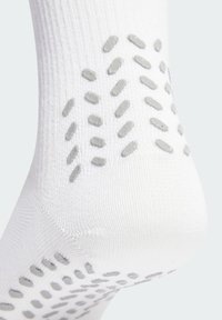 Talón de calcetín blanco con múltiples puntos de agarre de silicona gris antideslizante dispuestos en un patrón disperso para mejorar la tracción y la comodidad.