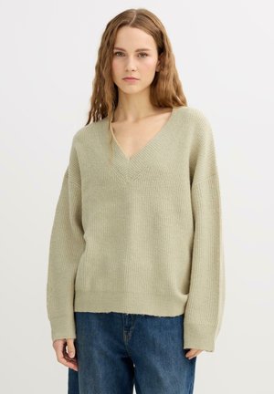 Suéter de punto acanalado verde claro con escote en V, hombros caídos y dobladillo recto. Combinado con vaqueros de mezclilla azul de pierna ancha.