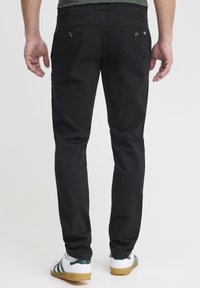 Czarne bawełniane spodnie o wąskim kroju, z dwoma tylnymi kieszeniami i gładką fakturą, zestawione z białymi sneakersami z zielonymi akcentami.