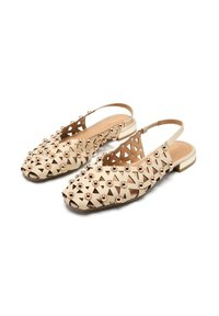 Beżowe płaskie buty typu slingback z wyciętym geometrycznym wzorem, ozdobione metalowymi ćwiekami, z małym obcasem i przezroczystym paskiem.