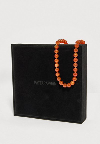 Colier portocaliu cu mărgele așezat peste o cutie pătrată neagră cu text subtil „PATTARAPHAN” pe față, pe un fundal alb.