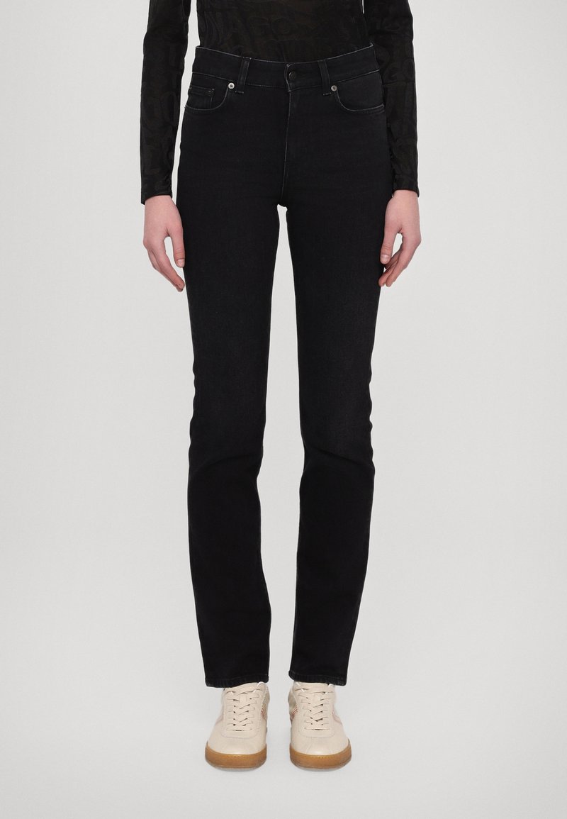 Jeans de mezclilla negros con cintura ajustada, piernas rectas y diseño de cinco bolsillos. Combinados con zapatillas color beige con suela blanca.