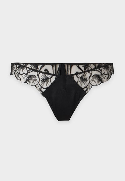 String en dentelle noire avec broderie florale et panneau avant en tissu uni sur fond gris clair.