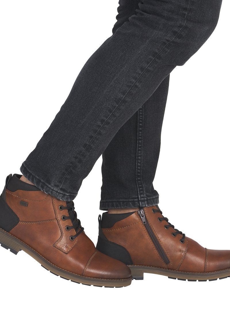 Bottines en cuir marron avec des accents noirs, dotées d'un laçage à l'avant, d'une fermeture éclair latérale et de semelles en caoutchouc texturé.