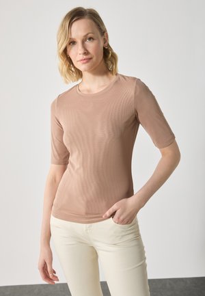 Haut beige à manches courtes en tissu lisse avec une coupe ajustée. Encolure ronde et texture subtile, associé à un pantalon de couleur claire.