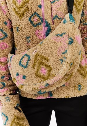 Beige fleece tas met kleurrijke geometrische patronen in roze, blauw en groen. Heeft een gebogen vorm, een ritssluiting en een zwarte schouderband.