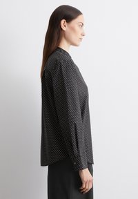 Schwarze Bluse mit Pünktchenmuster, strukturiertem Kragen, langen Ärmeln und geknöpften cuffs, aus einem leichten Stoff gefertigt. Seitenansicht gezeigt.