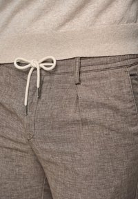 Brown linen blend pants featuring a drawstring waist with silver hardware. The fabric has a textured appearance.