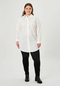 White, long-sleeve button-up shirt with a collared neck, curved hem, worn with black skinny jeans and ankle boots. Clean design, no patterns.