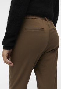 Brune skreddersydde bukser med en jevn tekstur, med to baklommer og elastisk midje, kombinert med en svart strikkegenser.