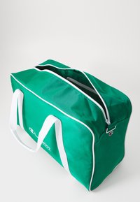 Bolsa de viaje de tela verde con acentos blancos, cierre con cremallera y asas dobles. Presenta un logo impreso en blanco en un lado.
