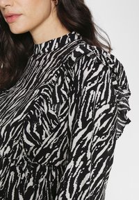 Blusa em preto e branco com padrão de riscas de zebra, detalhes de babados nos ombros, gola alta e textura de tecido suave.
