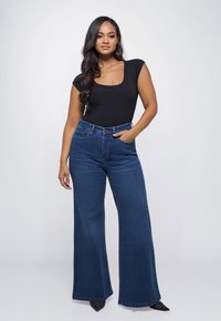 Zwarte top met ronde hals, gecombineerd met high-waisted, wijdvallende blauwe denim jeans, voorzien van een klassiek vijf-pocket ontwerp en subtiele stikselaccenten.