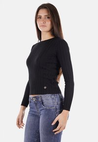 Maglione nero a maniche lunghe con scollatura rotonda e vita aderente, dotato di un piccolo logo metallico in basso.