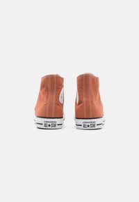 Baskets montantes en toile couleur rouille avec des coutures blanches, bout arrondi et semelle en caoutchouc noire arborant la marque "Converse All Star".