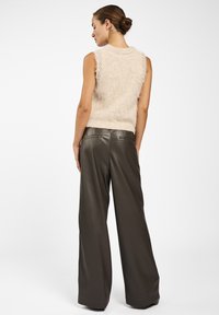 Beige fuzzy mouwloze sweater en high-waisted, wijdvallende donkerbruine leren broek. Zachte textuur met ribbelranden. Eenvoudig, strak ontwerp.