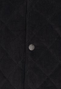 Fekete kordbársony dzseki steppelt mintával, ezüst gombbal. A textúrája bordázott, függőleges vonalakkal, mélységet és dimenziót teremtve.