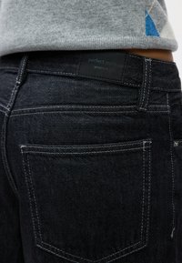 Črne jeans hlače iz denima s zadnjo zasebno nalepko z napisom "perfect jeans" in "ginatricot." Bele šivane podrobnosti na žepih in šivih.