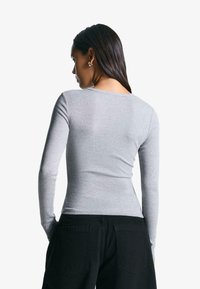 Langärmliges graues Oberteil mit rundem Ausschnitt, figurbetonter Passform und weicher Textur, kombiniert mit schwarzen, hochgeschnittenen Cargo-Hosen mit aufgesetzten Taschen.