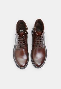 Botas de piel marrón hasta el tobillo con un acabado suave, que cuentan con cordones, un cierre lateral de cremallera y un diseño de punta redonda. Detalles de costura sutil en toda la bota.