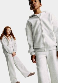 Lysegrå hættetrøje og matchende sweatpants lavet af blødt stof med en afslappet pasform; har en fuld lynlås og sidelommer.