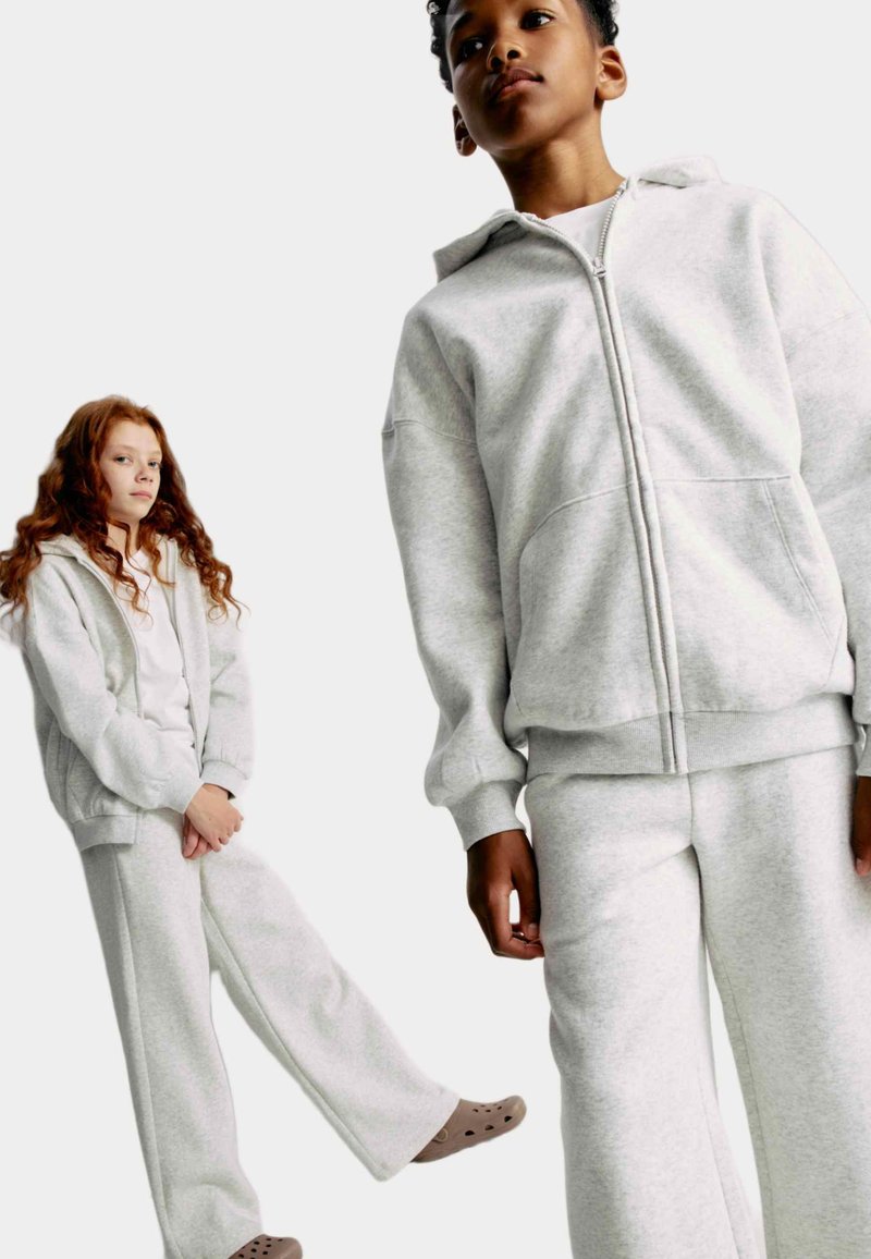 Lysegrå hættetrøje og matchende sweatpants lavet af blødt stof med en afslappet pasform; har en fuld lynlås og sidelommer.