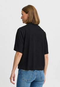 Sort kortærmet top med ribbet tekstur og båndkrave, der har en afslappet pasform og lige kant, parret med blå jeans.