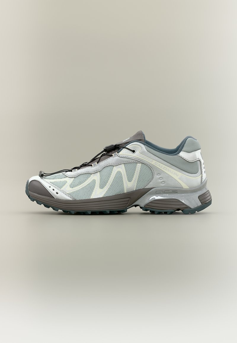 Sivo-bela nizka tekaška obutev za steze z mrežastimi paneli, nastavljivim zateznim vezalkami in robustnim podplatom za zunanjo uporabo.