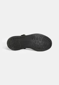 Schwarze Gummisohle mit einem strukturierten Profilmuster, das Rillen und Punkte für besseren Halt aufweist, sowie einer verstärkten Seitenkante.