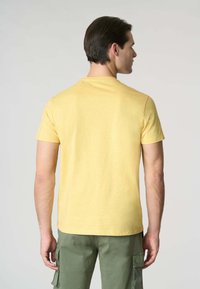 T-shirt giallo in cotone con maniche corte e scollatura rotonda, abbinato a pantaloni cargo verde oliva, la trama del tessuto appare morbida.