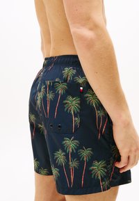 Shorts de bain navy avec imprimé palmier, dotés d'une taille élastique et d'une poche arrière avec deux œillets. Texture légère et lisse.